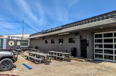 A brown warehouse type building with benches outside and a sign that says Fly Llama Brewery.