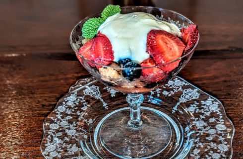 Colorful mixed fruit with a dollop of yogurt, garnished with a piece of green mint, in a crystal fruit bowl on a crystal plate.
