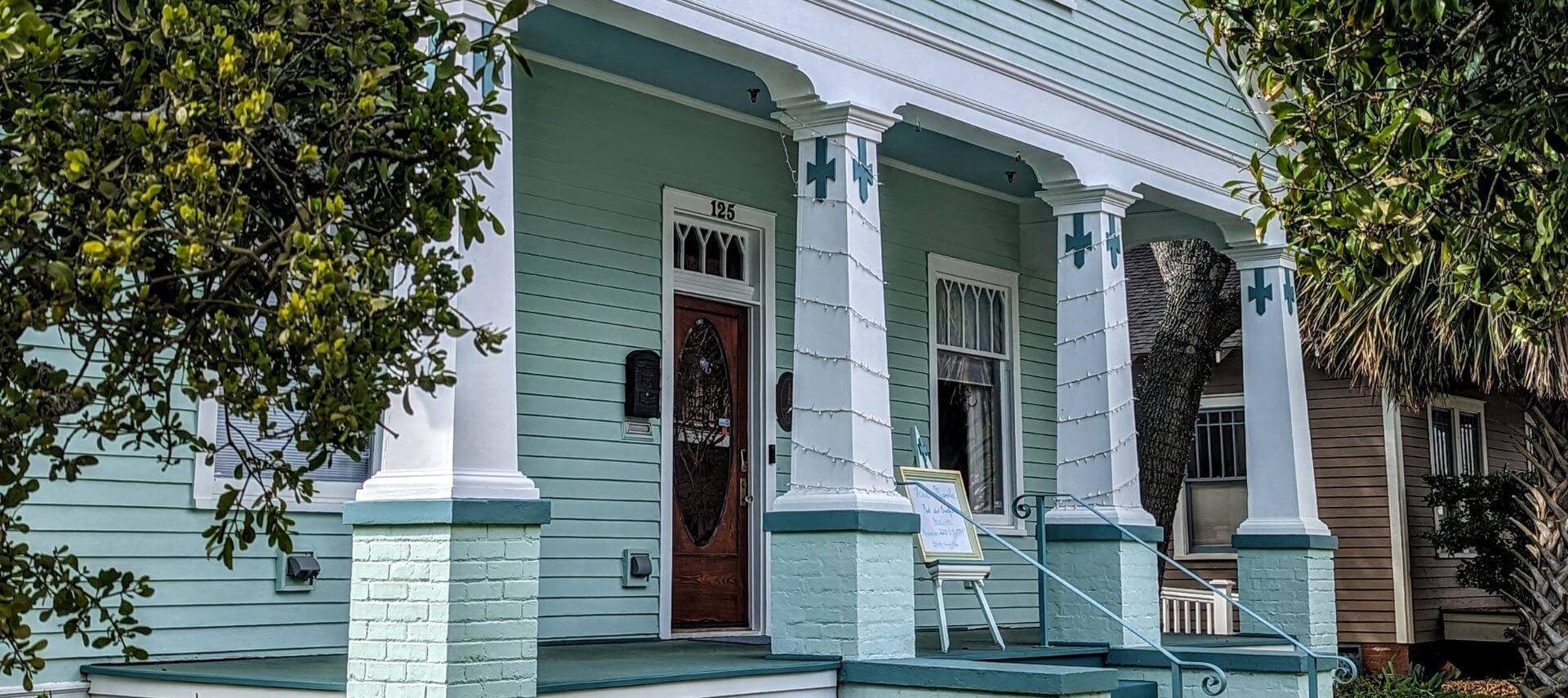 A green Victorian house's front porch with green and white pillars